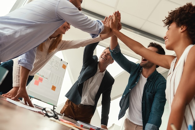 Conseguimos. Executivos dando cumprimentos uns aos outros e sorrindo enquanto trabalhavam juntos em um escritório moderno. Trabalho em equipe. Sucesso