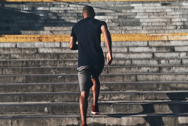 Conseguir mejores resultados. Vista trasera del joven africano en ropa deportiva corriendo por las escaleras mientras hace ejercicio al aire libre