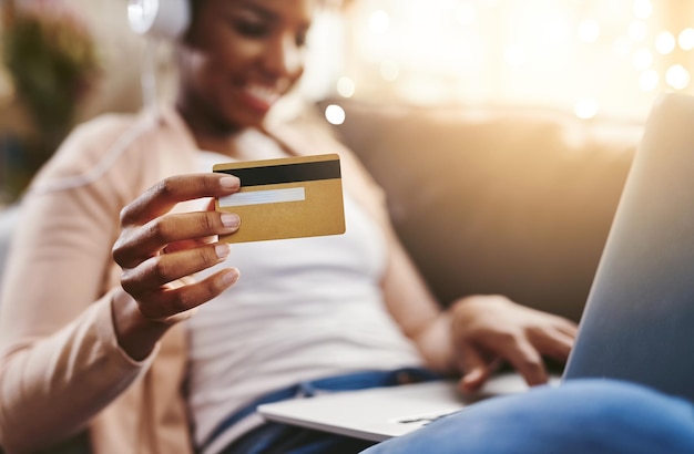 Conseguir música nueva nunca ha sido tan fácil Fotografía de una mujer joven irreconocible comprando en línea mientras se relaja en el sofá de su casa