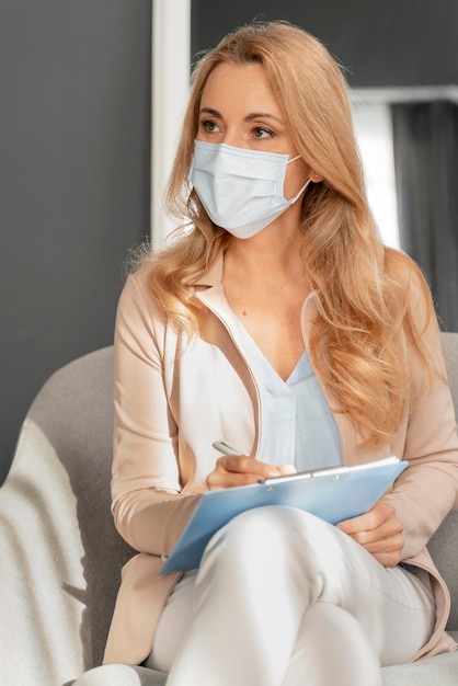 Consejero de mujer de tiro medio con mascarilla escuchando al paciente