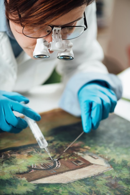 Foto conservador restaurando una vieja pintura al óleo revitalizando el lienzo con una jeringa