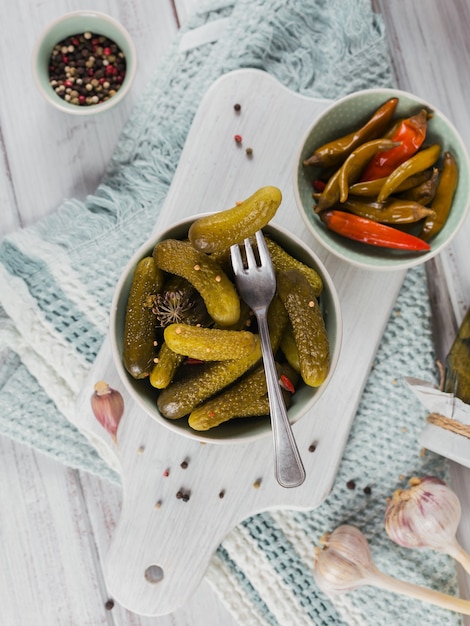 Conservando pepinos em conserva, pimenta, temperos e alho em uma mesa de madeira branca