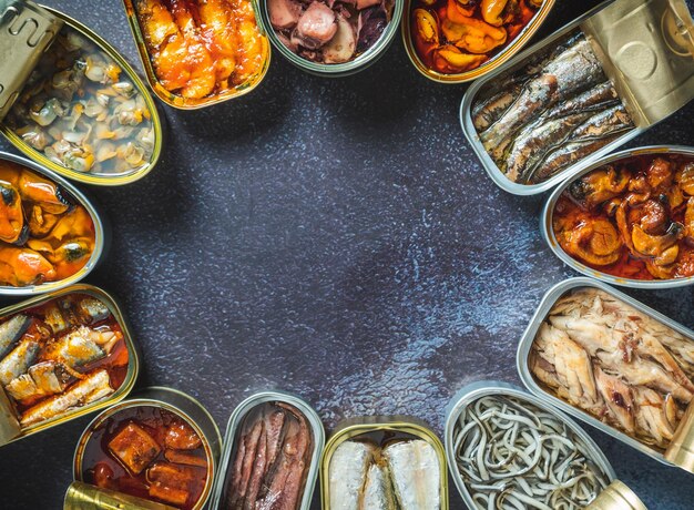 Conservar latas com diferentes frutos do mar abertas em uma mesa escura