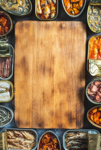 Foto conservar latas con diferentes productos de pescados y mariscos abiertos sobre una mesa oscura