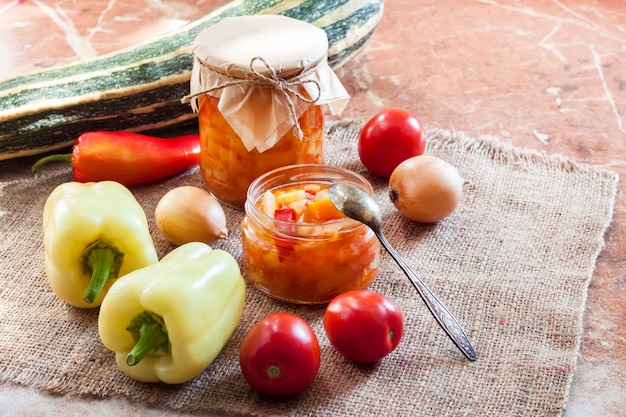 Conservas caseiras. Salada de abobrinha e pimentão em frasco de vidro com ingredientes no fundo