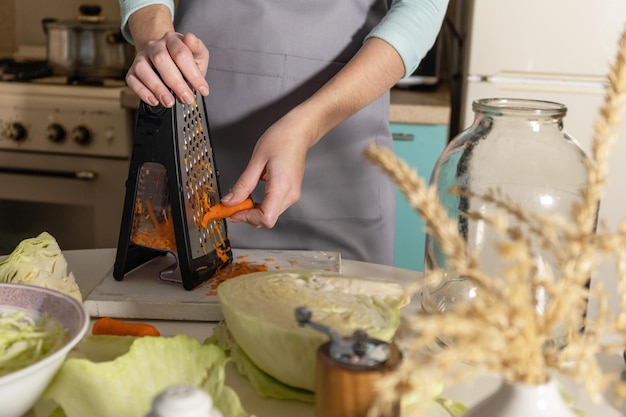 Conservas de chucrut Una mujer joven prepara chucrut casero con zanahorias en la cocina