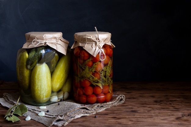 Conservas de pepinos e tomates em uma jarra sobre uma mesa de madeira