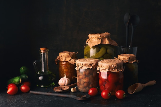 Conservas de frutas y verduras. Frascos de vidrio con frutas y verduras fermentadas, en escabeche y enlatadas en la mesa de la cocina rústica oscura.