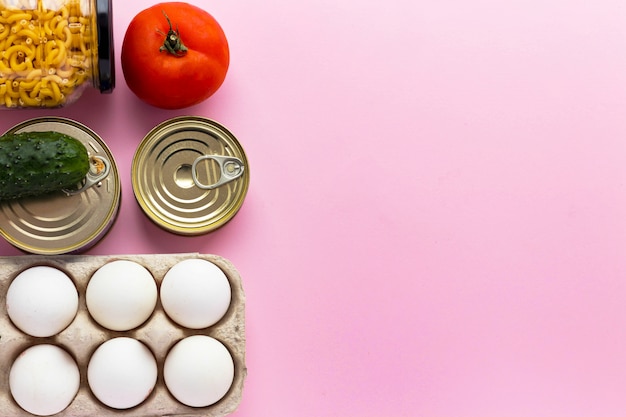 Conservas, legumes frescos, tomate e pepino, ovos de galinha e macarrão em frasco de vidro no fundo rosa