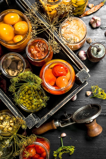 Conservas de verduras y setas en una caja con cerradora en pizarra negra.