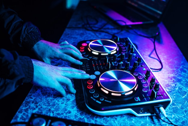 Foto consola de dj para mezclar música con las manos y con gente borrosa bailando en una fiesta de club nocturno