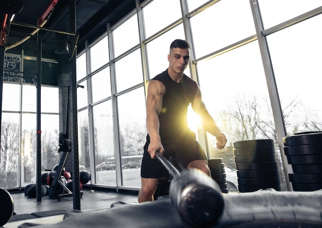 Construa você mesmo. Jovem atleta caucasiano musculoso treinando no ginásio, fazendo exercícios de força, praticando, trabalhando na parte superior do corpo com pesos e martelo. Fitness, wellness, conceito de estilo de vida saudável.