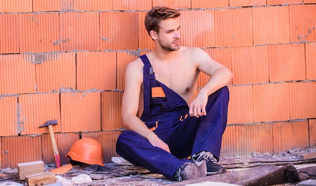 Construção civil. homem constrói sua própria casa. trabalhador atraente. trabalhador bonito e sexy. inspecionando edifício. reparação de trabalhador de reparação de manutenção geral, manutenção do edifício. fundo da parede de tijolo do trabalhador.