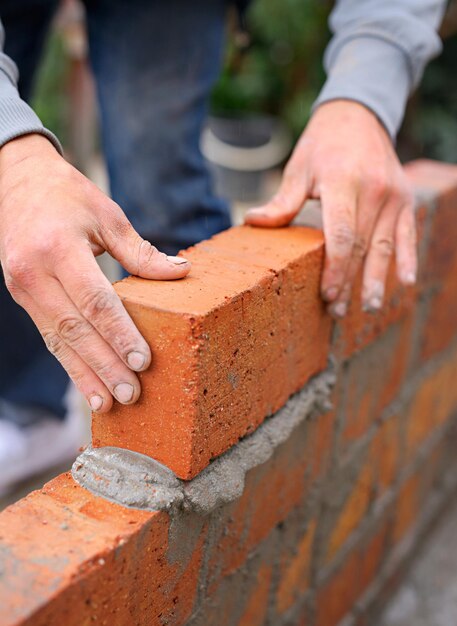 Foto construção de edifícios e pedreiro com as mãos e cimento empilhado tijolos para fundação de parede trabalhador industrial artesão ou alvenaria para manutenção com empreiteiro projeto no local com capataz