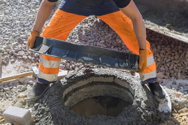 Construção de esgoto com um trabalhador de serviço público instalando poço subterrâneo de esgoto de bueiro