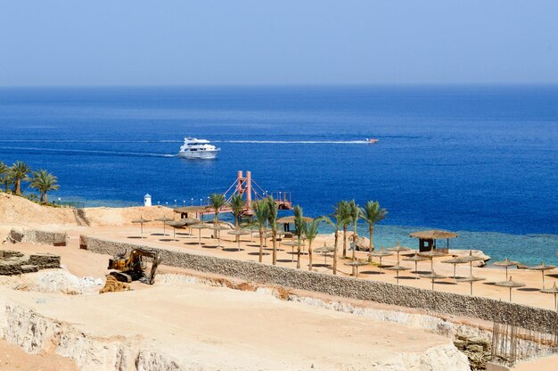 Construção de um hotel no deserto em um resort de férias exótico do sul tropical quente contra um mar azul de palmeiras e navios brancos