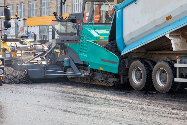 Foto construção de uma nova estrada um caminhão despeja asfalto quente no balde de um pavimentador de asfalto em close-up