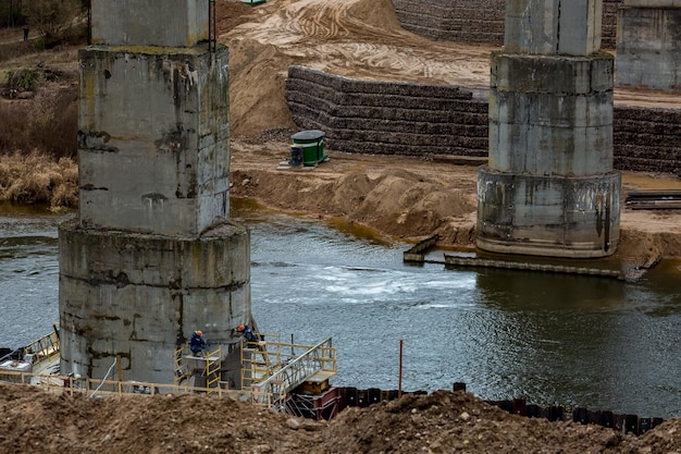 Construção ou reconstrução de ponte de concreto de rodovia sobre um grande rio trabalho de caminhões e guindastes de máquinas de construção