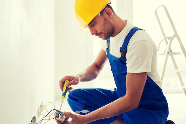 Foto construcción, renovación, tecnología, electricidad y concepto de personas - constructor con enchufe de fijación de destornillador en interiores