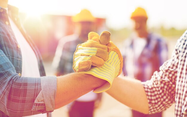 Foto construcción, trabajo en equipo, asociación, gesto y concepto de personas: cierre de las manos de los constructores con guantes saludándose con un apretón de manos en el sitio de construcción