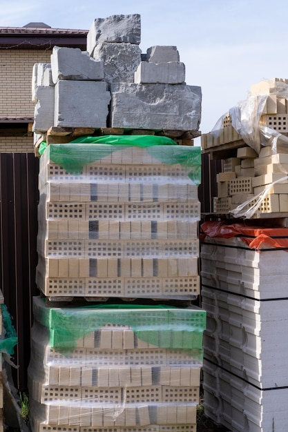 Construcción de viviendas Bloques de hormigón y ladrillos marrones para construir una casa apilados en varias filas sobre palets de madera marco vertical El material de construcción se apila sobre un palet de madera