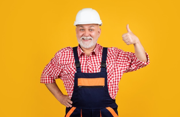 Constructor de anciano feliz en casco sobre fondo amarillo pulgar arriba