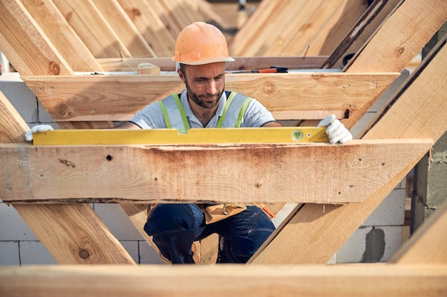 Constructor atento utilizando una herramienta de nivel de burbuja mientras mide una superficie de madera de un techo