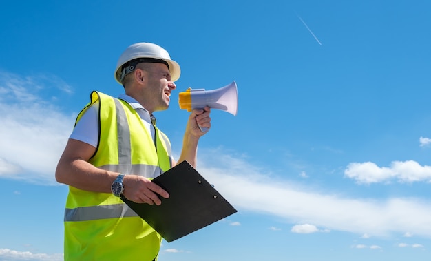 Constructor en un casco blanco grita en un megáfono contra un fondo de cielo azul