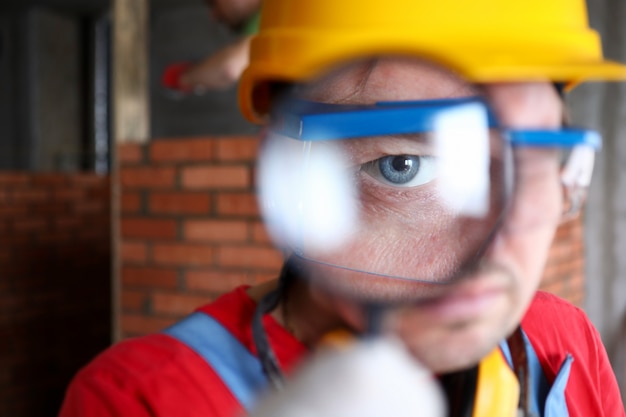 Foto constructor en casco mira a través del retrato de lupa
