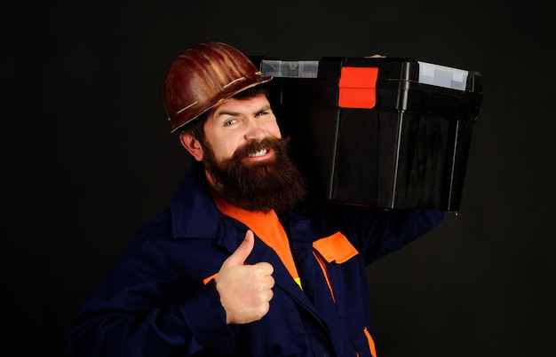 Constructor en casco protector con caja de herramientas muestra herramientas de pulgar hacia arriba para reparar reparador en uniforme con