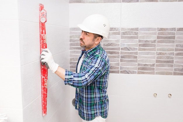 Un constructor con un casco de seguridad comprueba la uniformidad de un azulejo en un baño durante una renovación