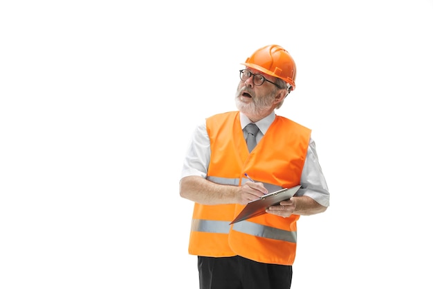 El constructor en un chaleco de construcción y casco naranja de pie sobre fondo blanco de estudio. Especialista en seguridad, ingeniero, industria, arquitectura, gerente, ocupación, empresario, concepto de trabajo