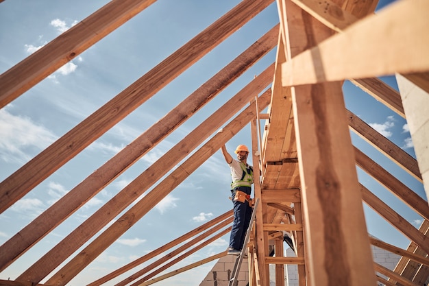 Constructor competente con casco mientras se sube en los escalones y se apoya en las vigas