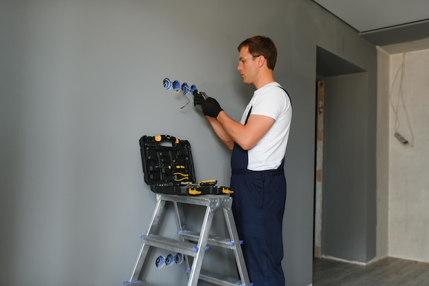 Foto constructor de electricista en el trabajo instalación de enchufes e interruptores profesional en overoles con una herramienta de electricista en el contexto del sitio de reparación