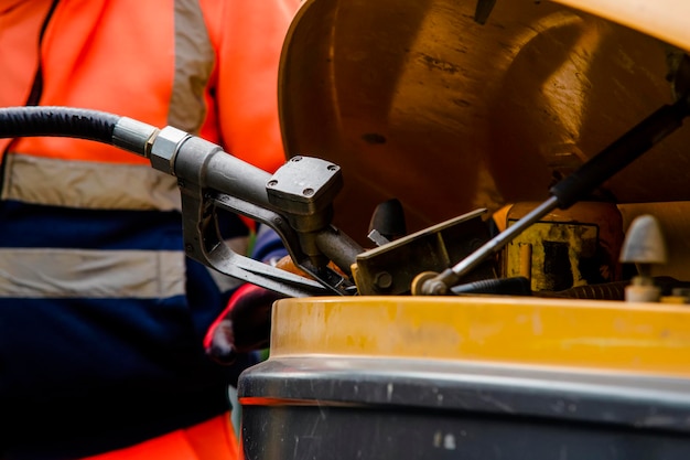 Constructor en guantes de seguridad que llenan la excavadora con combustible diesel en el sitio de construcción