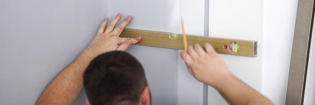 Un constructor de hombres marca una línea en la pared con un nivel de construcción preparando la pared para colocar