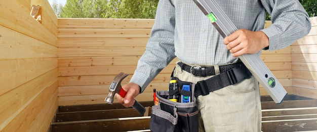 El constructor mantiene el nivel y el martillo en la casa de madera de fondo para la construcción