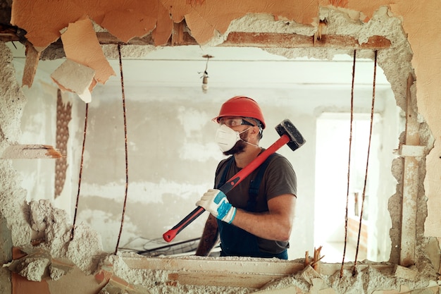 Foto constructor con un martillo en sus manos rompe la pared de cemento