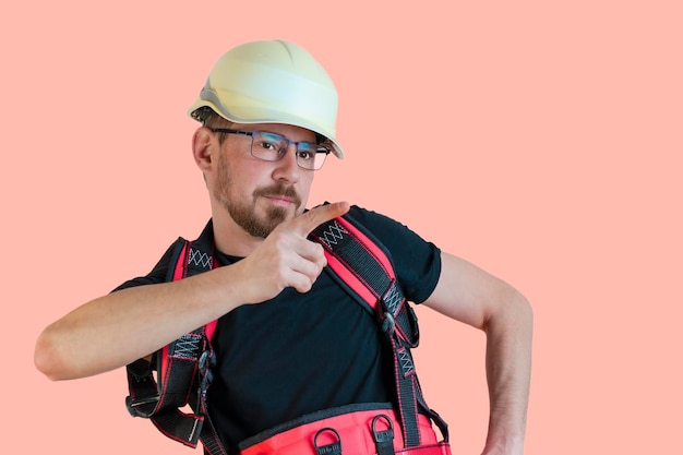 Constructor masculino barbudo amigable positivo en overoles y casco de seguridad y gafas mirando a la cámara sobre fondo aislado