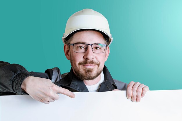 Constructor masculino barbudo amistoso positivo en casco de seguridad y gafas que apuntan al espacio publicitario Fondo pastel aislado Mocap para texto