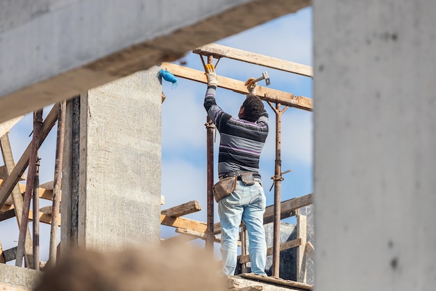 Un constructor masculino construye un edificio martillando un clavo mientras está parado en una construcción especial. Reconstrucción de un edificio antiguo