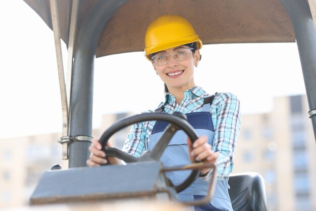 Constructor de mujer sonriente en casco de conducción de equipos de construcción