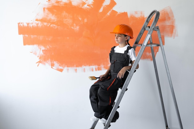 Constructor de niña vestida con ropa de constructor y un casco naranja en la cabeza. sentado en las escaleras durante el descanso.