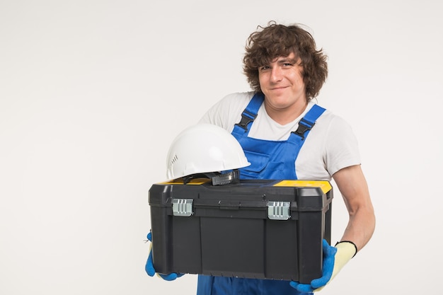 Constructor de pelo rizado levantando caja de herramientas y casco blanco en estudio.