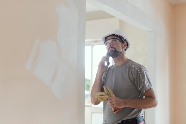 Constructor profesional con casco de seguridad con una llamada telefónica de renovación del hogar y concepto de comunicación