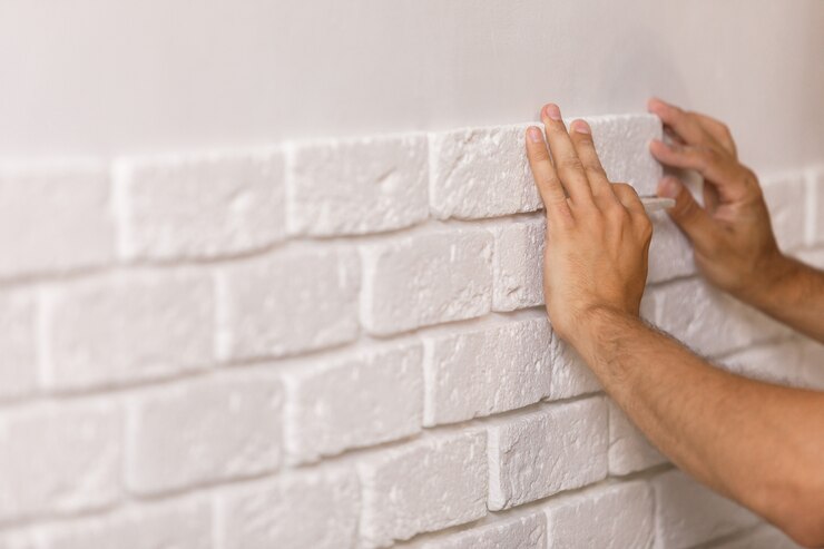 Constructor profesional pegando baldosas decorativas en la pared. Trabajador monta ladrillos decorativos en la pared