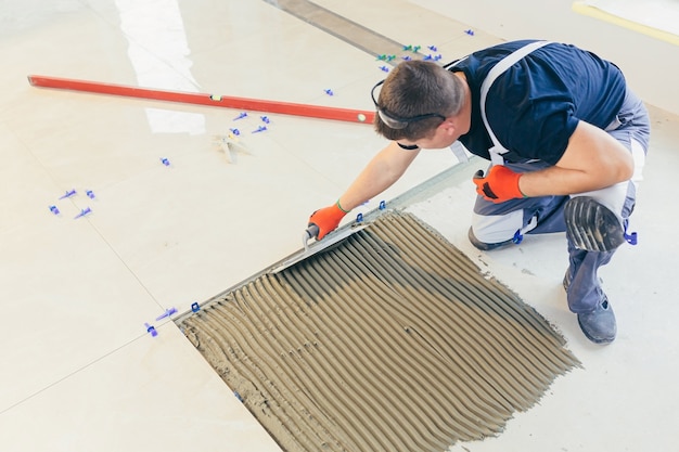 un constructor que instala el piso con grandes baldosas de cerámica durante los trabajos de reparación