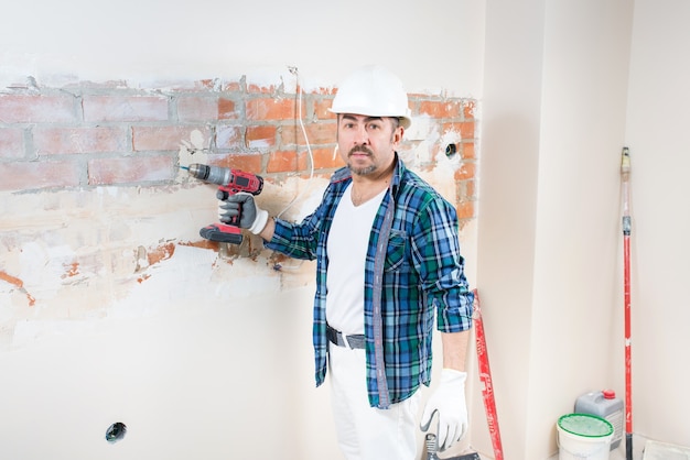 Un constructor-reparador en un casco protector tiene un destornillador eléctrico en su mano