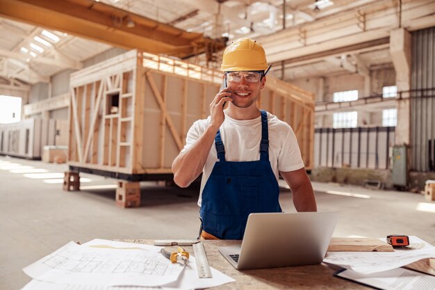 Constructor de sexo masculino alegre que habla en el teléfono celular en el trabajo