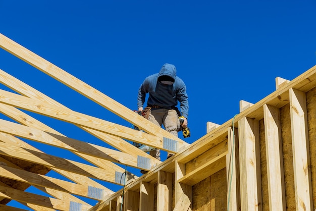 El constructor en el techo sin terminar con vigas de madera clavadas en una casa de madera en construcción